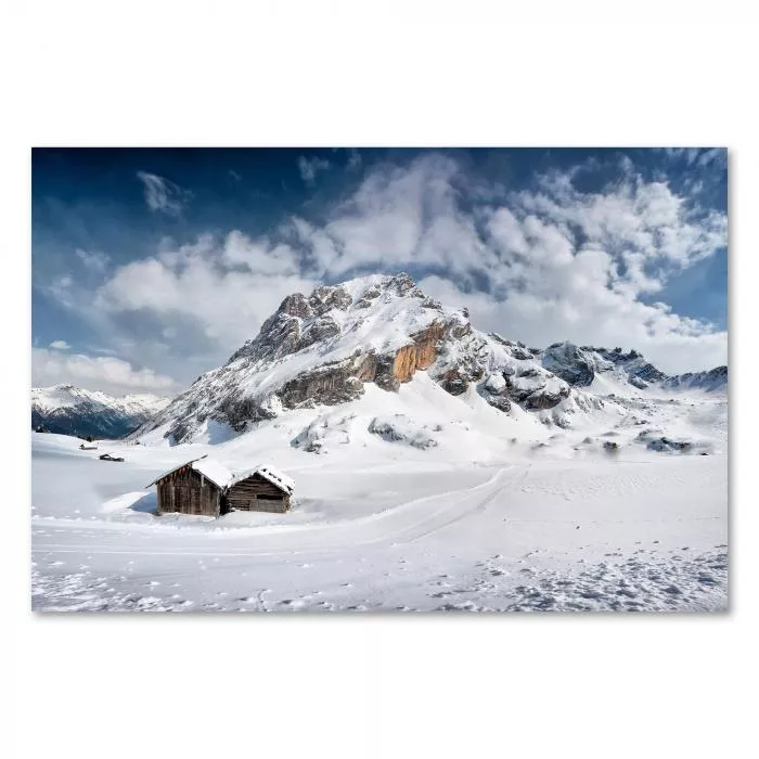 Atemberaubendes Alpenpanorama mit einsamer Berghütte, Schnee und tiefblauen Wolken schaffen Winteratmosphäre.